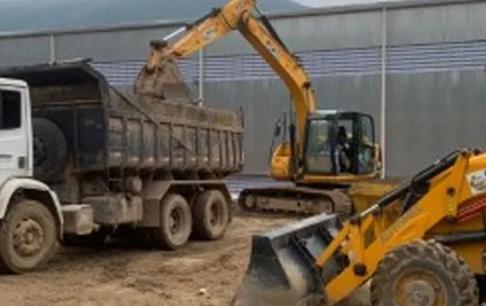 Caminhão basculante e retroescavadeira em serviço de terraplenagem